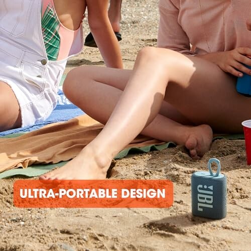 People relaxing on a beach with a JBL portable speaker.