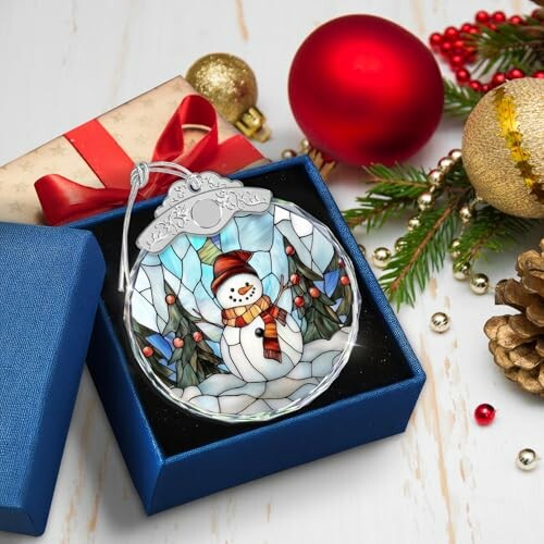 Stained glass snowman ornament in a gift box with Christmas decorations.