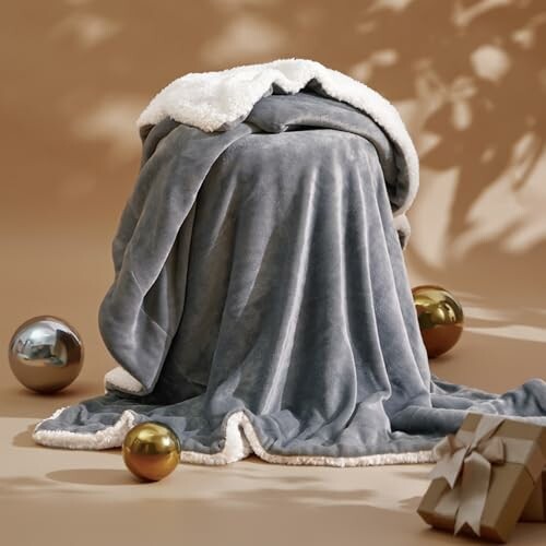 Soft gray blanket draped over a surface with decorative balls and a wrapped gift on a brown background.
