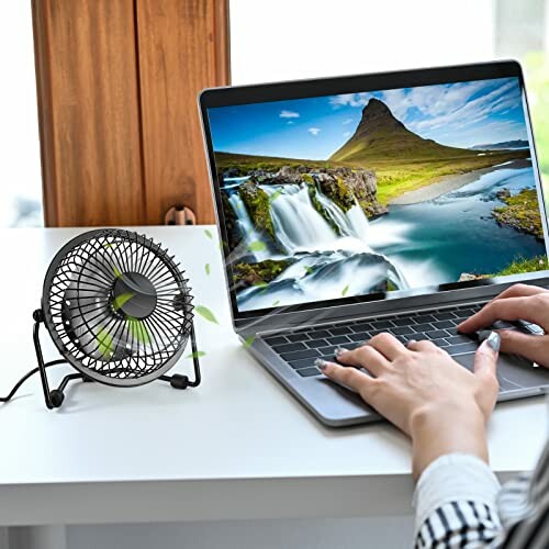 Person typing on laptop next to small desk fan