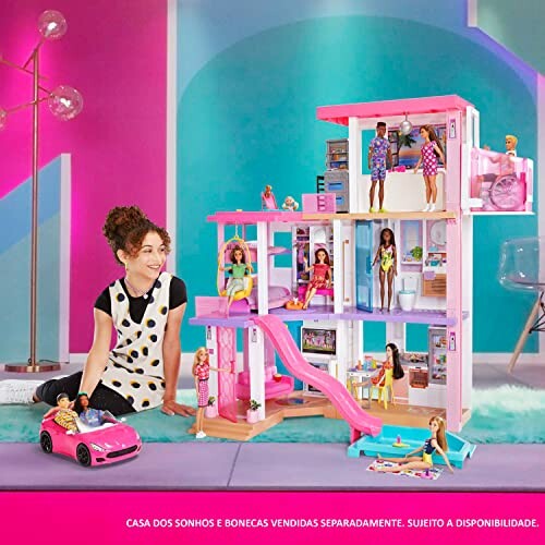 Child playing with a large colorful dollhouse and dolls. The Barbie Convertible 2-Seater Vehicle is in the background with the dolls inside it.