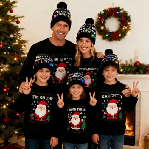 Family in matching Christmas sweaters and hats by a decorated tree and fireplace.