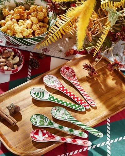 Colorful festive spoons on a wooden tray with popcorn and nuts on a table.