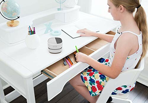 Girl sitting at a white desk writing in a notebook with colored pencils and a globe.