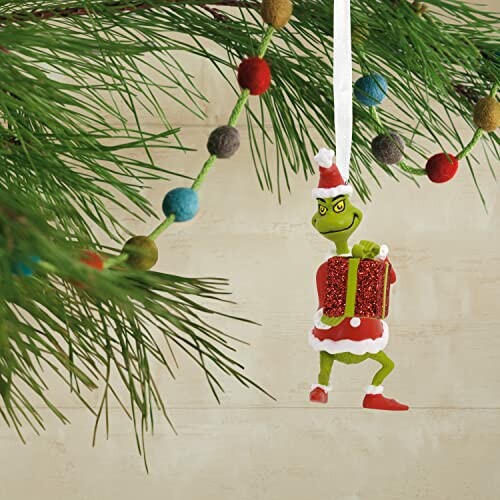 Grinch Christmas ornament hanging on a pine branch.