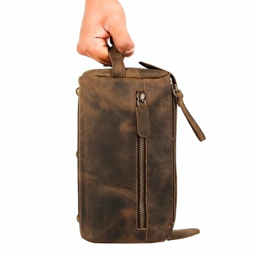 Hand holding a brown leather toiletry bag with zipper
