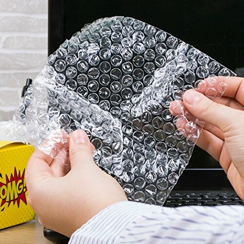 Hands holding bubble wrap in front of a laptop.