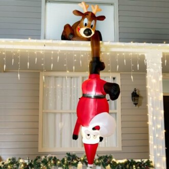 Inflatable Santa hanging upside down with reindeer on roof.