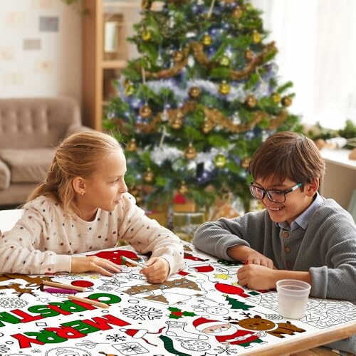Two children coloring a Christmas-themed tablecloth near a decorated Christmas tree.