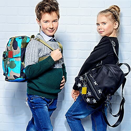 Two children posing with backpacks against a brick wall.