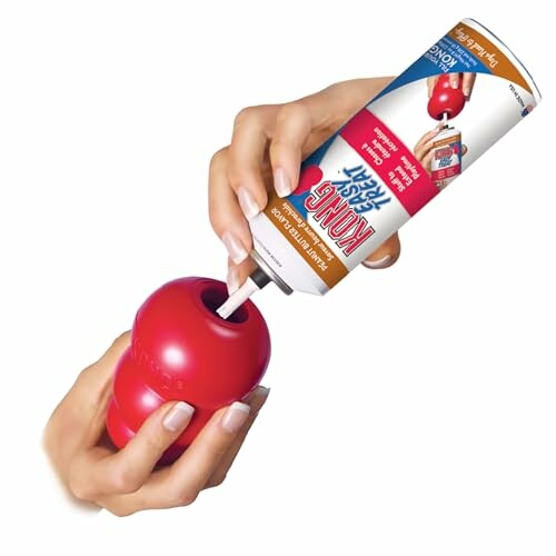 Hands filling a red KONG dog toy with a treat spray, showcasing the ease of use and versatility of the toy.