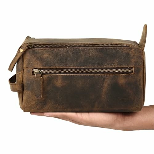 Hand holding a brown leather dopp kit with zipper pocket