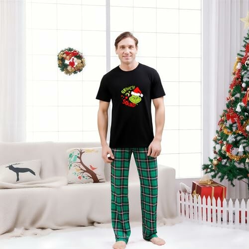 Man in Christmas pajamas standing in a decorated living room with a Christmas tree and wreath.