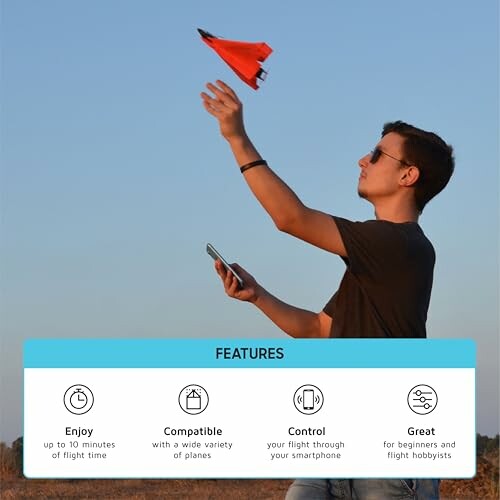 Man launching a paper plane outdoors with smartphone in hand.