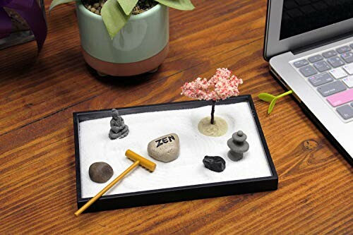 Mini Zen garden with sand, stones, tree, and Buddha statue on a desk.