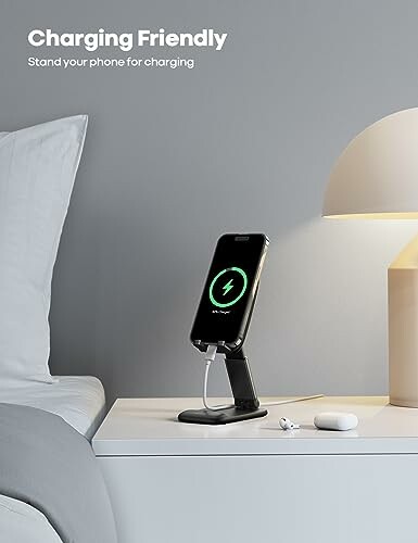 Phone on charging stand beside bed with lamp and earphones.