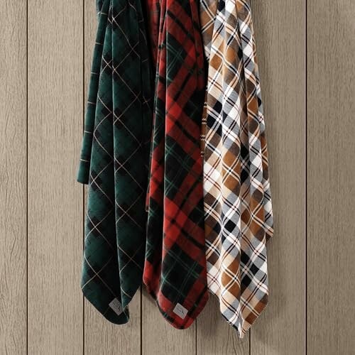 Three plaid patterned blankets hanging on a wall.