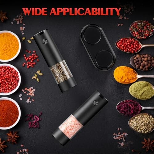 Spice grinders surrounded by various spices in bowls on a dark surface.