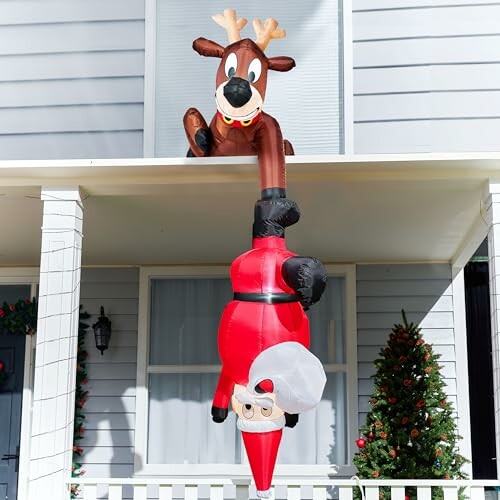 Inflatable Santa hanging upside-down with reindeer on porch.