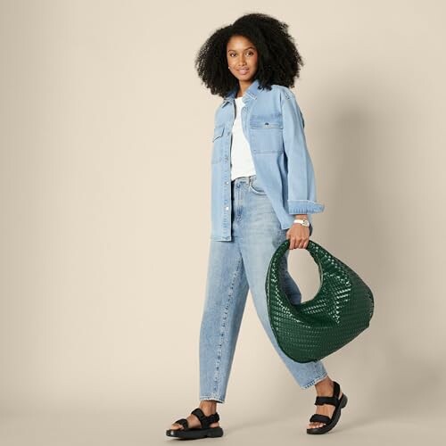 Woman in denim jacket and jeans holding a green bag.